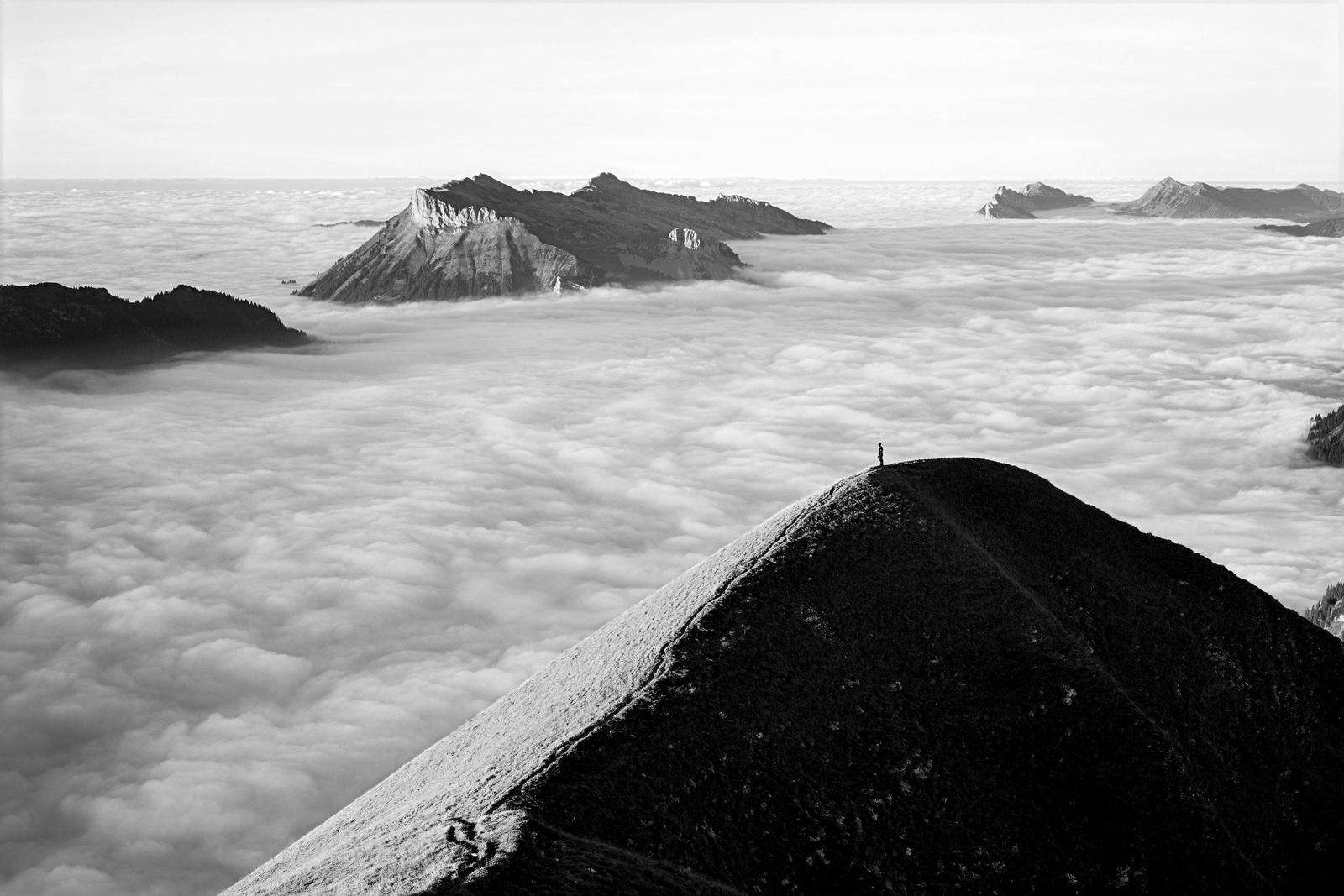 A climber on a dark ridge above a sea of clouds